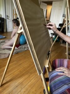 A person painting on an easel in the middle of a room.